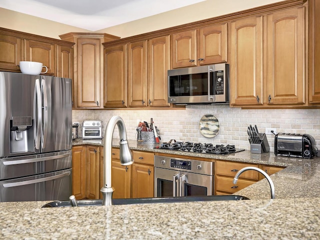 kitchen featuring light stone counters, brown cabinetry, a toaster, decorative backsplash, and appliances with stainless steel finishes