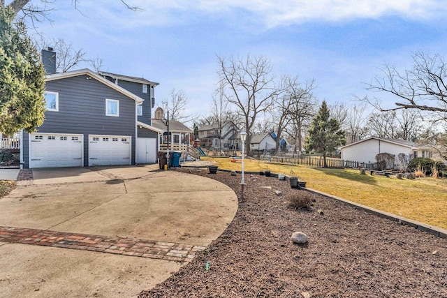 view of side of property with fence, a lawn, a chimney, driveway, and an attached garage