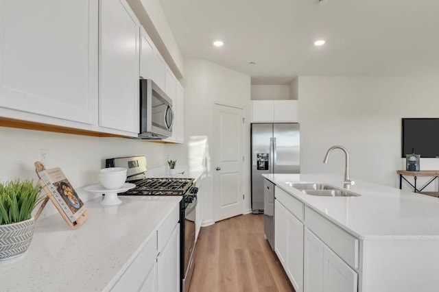 kitchen with light wood-style flooring, a center island with sink, a sink, white cabinetry, and appliances with stainless steel finishes