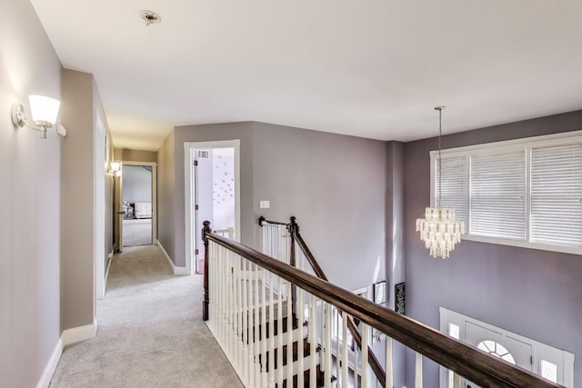 corridor featuring an upstairs landing, a notable chandelier, light colored carpet, and baseboards