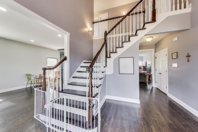 stairway featuring a high ceiling, recessed lighting, wood finished floors, and baseboards