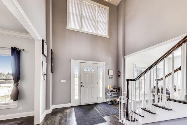 foyer entrance featuring baseboards, dark wood-style flooring, ornamental molding, stairs, and a towering ceiling