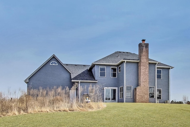 back of house with a chimney, a yard, and roof with shingles