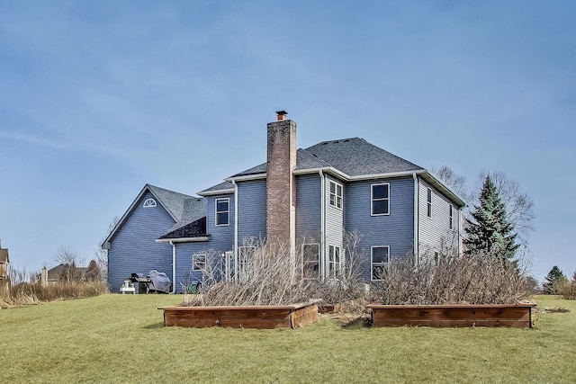 back of house featuring a chimney, a shingled roof, and a yard