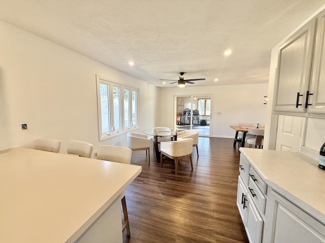 kitchen featuring dark wood finished floors, a kitchen bar, light countertops, a textured ceiling, and white cabinetry