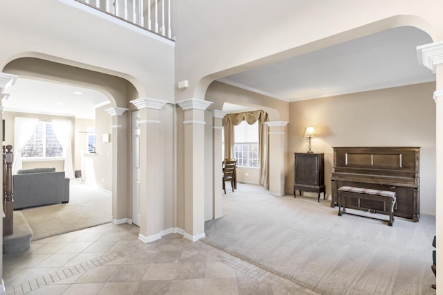 hall featuring decorative columns, arched walkways, ornamental molding, tile patterned flooring, and carpet flooring