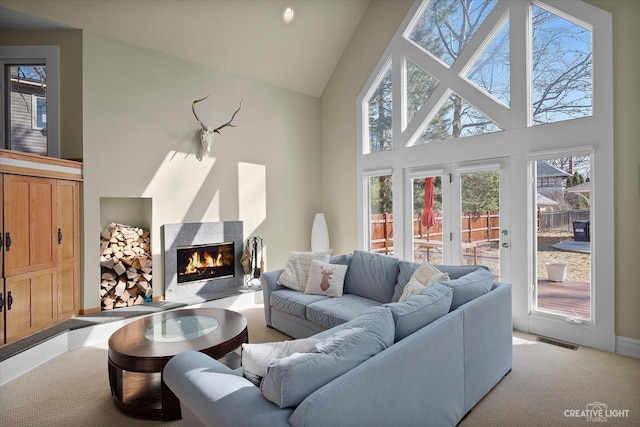 living room featuring a glass covered fireplace, visible vents, and high vaulted ceiling