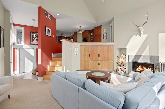 living area featuring a glass covered fireplace, light colored carpet, visible vents, and high vaulted ceiling