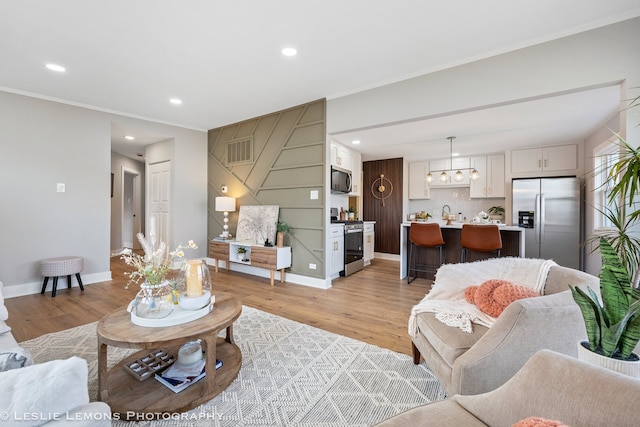 living room with visible vents, light wood-style flooring, ornamental molding, recessed lighting, and baseboards