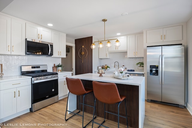 kitchen featuring a breakfast bar area, light wood-style flooring, light countertops, white cabinets, and appliances with stainless steel finishes