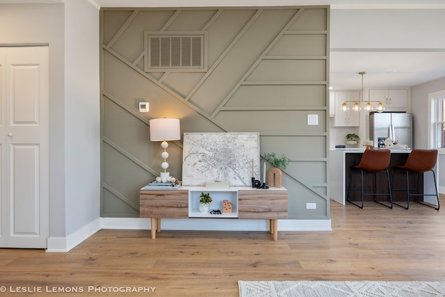 interior details with a chandelier, visible vents, freestanding refrigerator, and wood finished floors