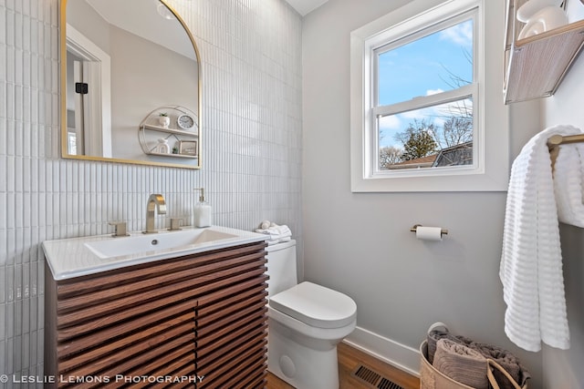 half bath with vanity, wood finished floors, visible vents, tile walls, and toilet