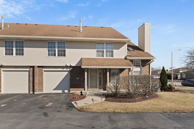 view of front of house with an attached garage, brick siding, driveway, and a chimney