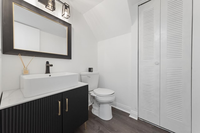 half bath with baseboards, toilet, lofted ceiling, wood finished floors, and vanity