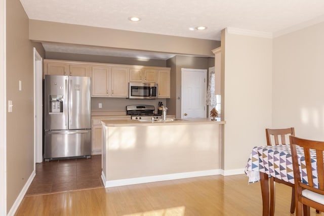 kitchen with light wood-style floors, appliances with stainless steel finishes, a peninsula, light countertops, and baseboards