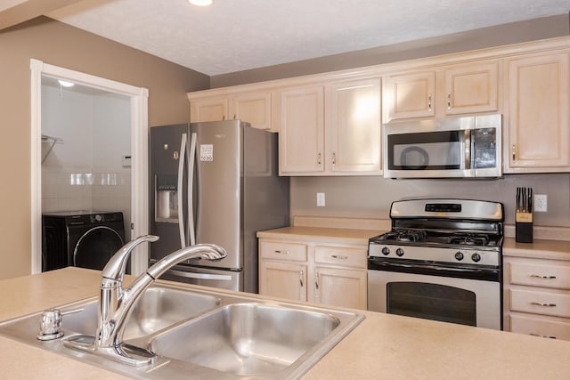 kitchen with washer / dryer, light countertops, appliances with stainless steel finishes, and a sink