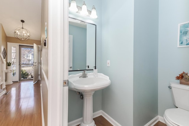 half bathroom featuring baseboards, toilet, an inviting chandelier, and wood finished floors