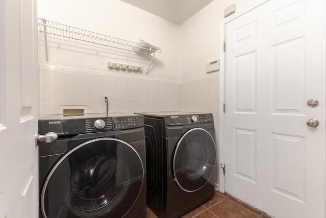 washroom featuring a wainscoted wall, dark tile patterned floors, washer and clothes dryer, tile walls, and laundry area