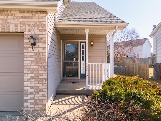 doorway to property with fence, roof with shingles, an attached garage, covered porch, and brick siding