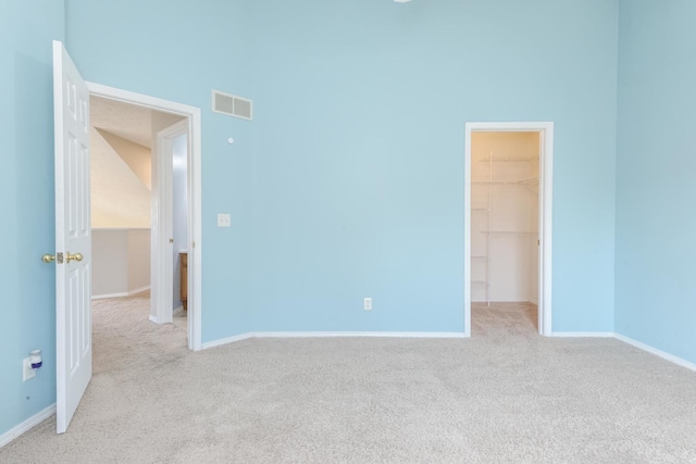 empty room featuring light colored carpet, visible vents, a towering ceiling, and baseboards