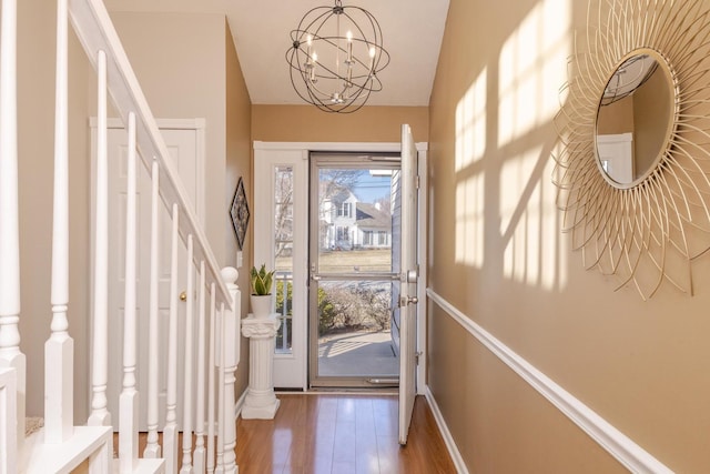 entrance foyer featuring baseboards, a chandelier, stairway, vaulted ceiling, and wood finished floors