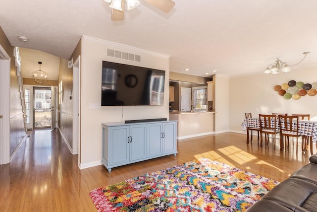 living area with ornamental molding, light wood-style floors, visible vents, and baseboards