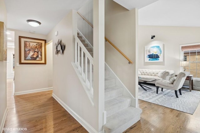 stairway featuring lofted ceiling, baseboards, and wood finished floors