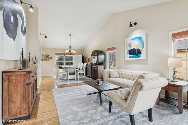 living room featuring baseboards, high vaulted ceiling, an inviting chandelier, and light wood-style flooring