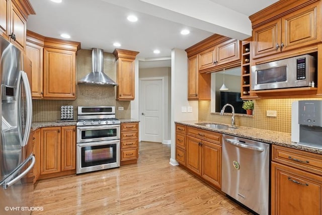 kitchen with a sink, stainless steel appliances, light wood-style floors, wall chimney range hood, and light stone countertops