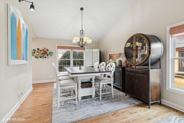 dining space featuring lofted ceiling, baseboards, light wood-style floors, and an inviting chandelier