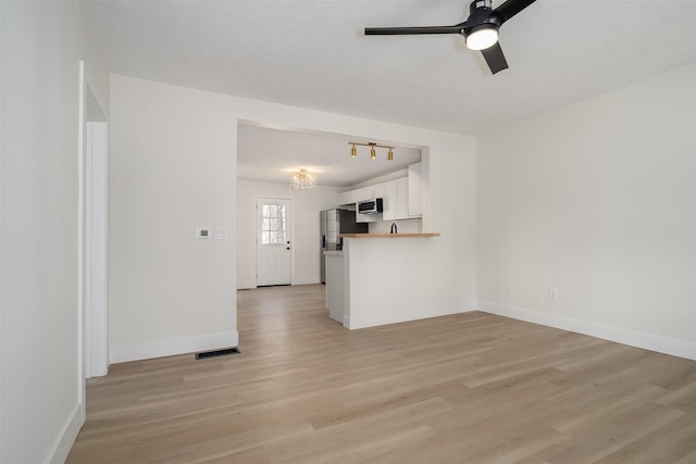 unfurnished living room with visible vents, baseboards, light wood-style flooring, and ceiling fan with notable chandelier