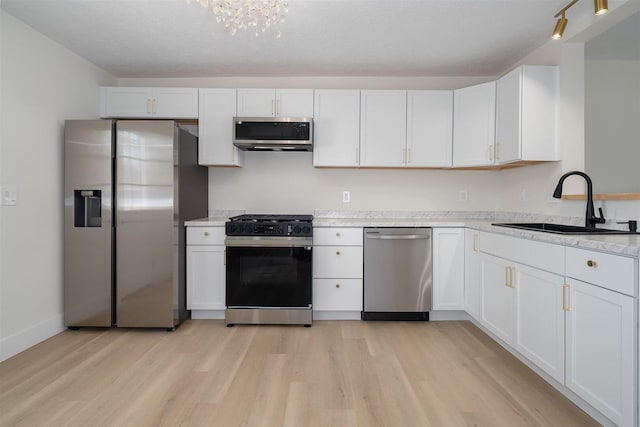 kitchen with light wood finished floors, baseboards, appliances with stainless steel finishes, white cabinets, and a sink