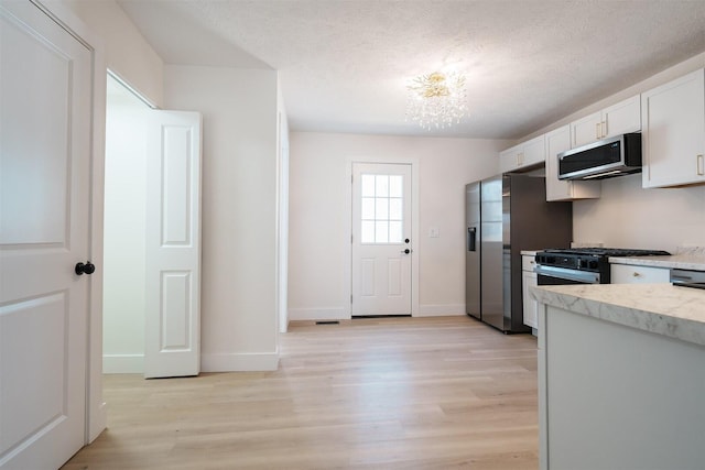 kitchen with stainless steel appliances, a notable chandelier, light wood-style flooring, and white cabinets