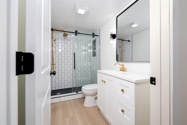 bathroom featuring toilet, a stall shower, wood finished floors, a textured ceiling, and vanity