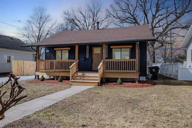 bungalow featuring a front yard, fence, covered porch, and a shingled roof