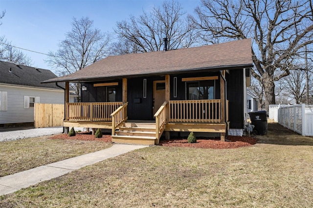 bungalow-style house featuring fence, covered porch, a front yard, and a shingled roof