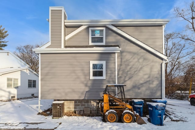 snow covered property with a chimney and central AC