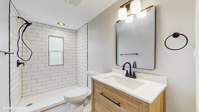 full bathroom with toilet, a tile shower, and vanity