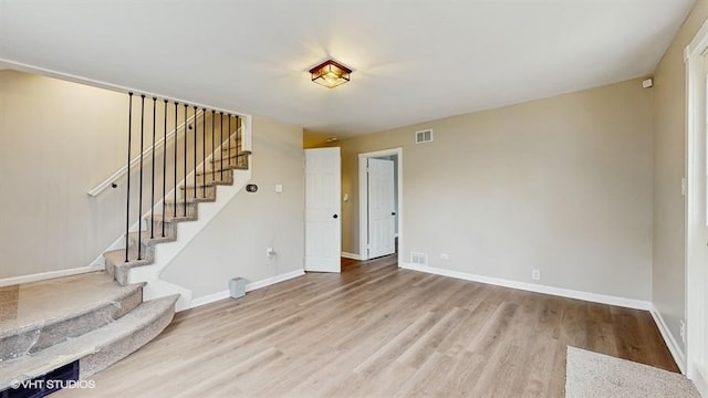 unfurnished living room featuring stairway, wood finished floors, and baseboards