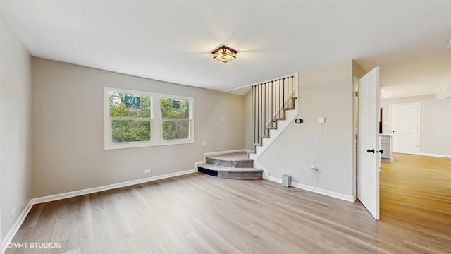unfurnished living room featuring light wood finished floors, stairs, and baseboards