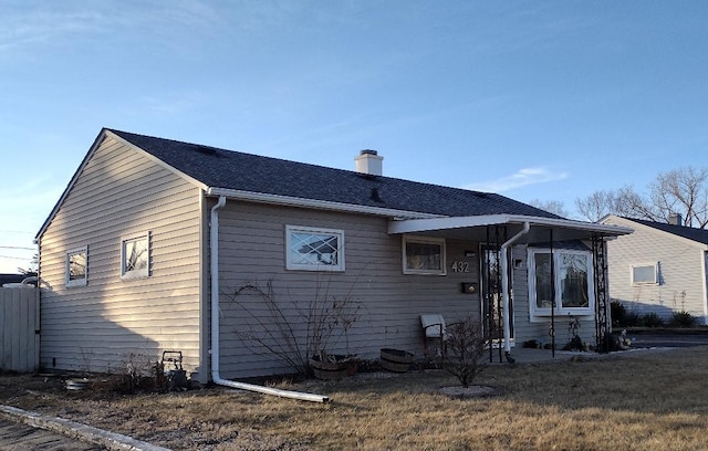 back of property with a shingled roof, a lawn, and a chimney