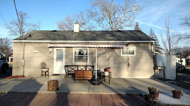 back of property featuring a chimney, a patio, and a shingled roof