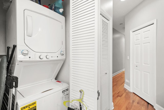 laundry room with laundry area, stacked washer / dryer, baseboards, and light wood-type flooring