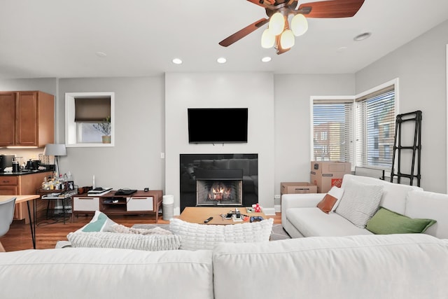 living room featuring baseboards, a lit fireplace, recessed lighting, wood finished floors, and a ceiling fan