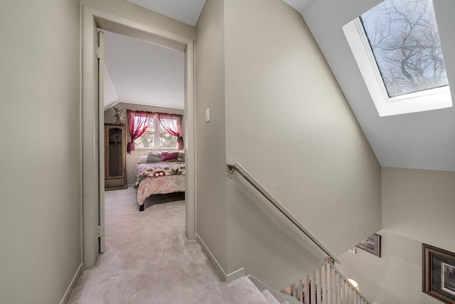 hall featuring lofted ceiling with skylight, an upstairs landing, baseboards, and light carpet