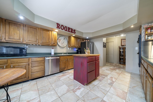 kitchen with a kitchen island, light tile patterned floors, appliances with stainless steel finishes, brown cabinetry, and a sink