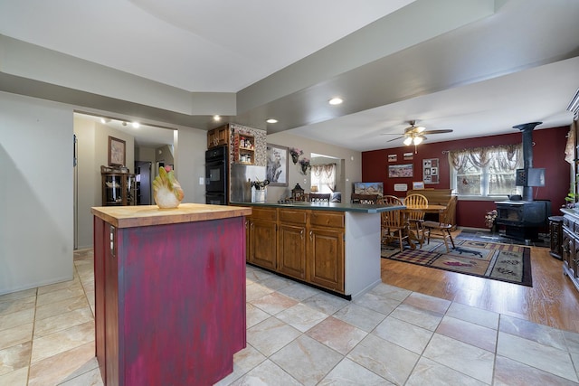 kitchen featuring a ceiling fan, wooden counters, a kitchen island, a wood stove, and dobule oven black