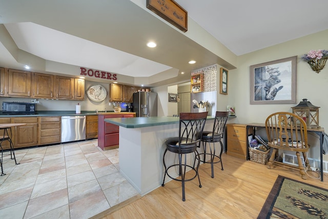 kitchen with a breakfast bar, a peninsula, a tray ceiling, stainless steel appliances, and brown cabinets