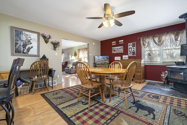 dining area featuring baseboards, a ceiling fan, wood finished floors, and a wood stove