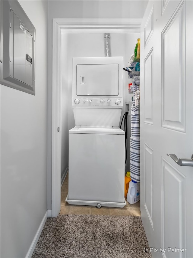 laundry area featuring laundry area, electric panel, baseboards, and stacked washer / drying machine